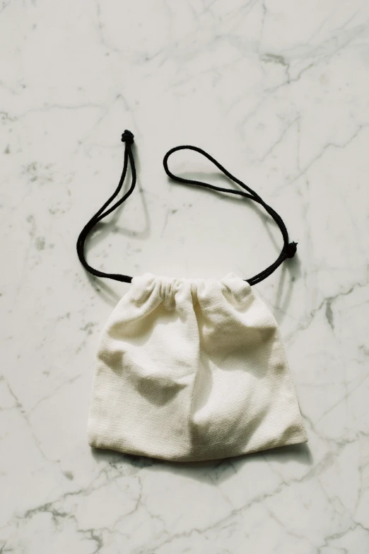 a white bag sitting on top of a marble counter, unsplash, renaissance, hair loops, ( ivory black ), front facing shot, cotton