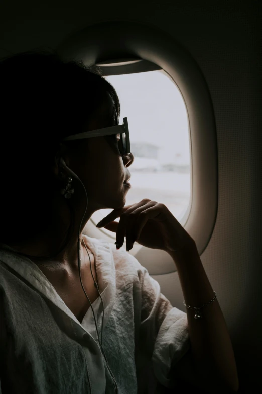 a woman sitting in an airplane looking out the window, pexels contest winner, ✨🕌🌙, wearing square glasses, facing away, wealthy women