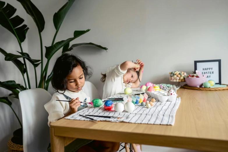 a couple of kids that are sitting at a table, inspired by Pacita Abad, pexels contest winner, wizard examining eggs, white paint, art toys, girls resting