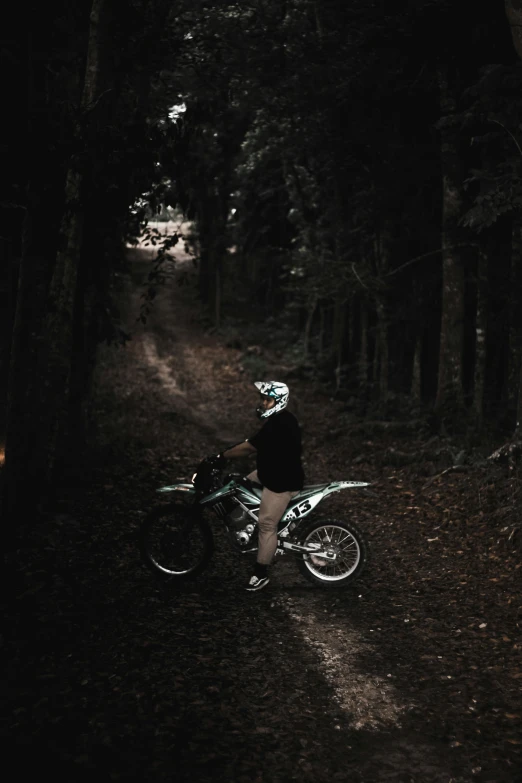 a man riding a dirt bike down a dirt road, standing in a dark forest, profile image