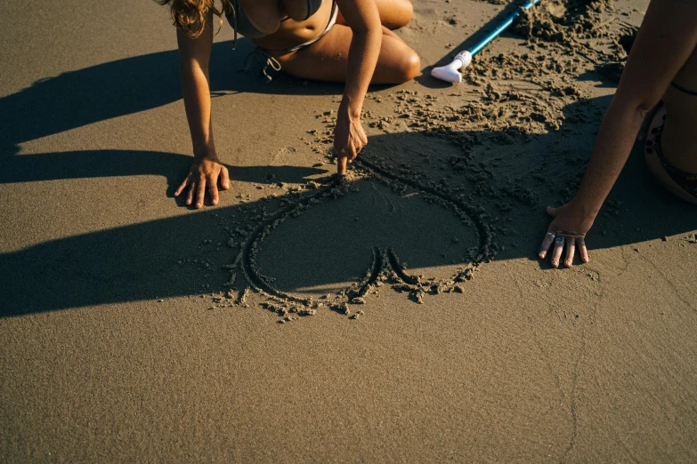 a couple of women sitting on top of a sandy beach, pexels contest winner, land art, entwined hearts and spades, drop shadow, sharpie, thumbnail