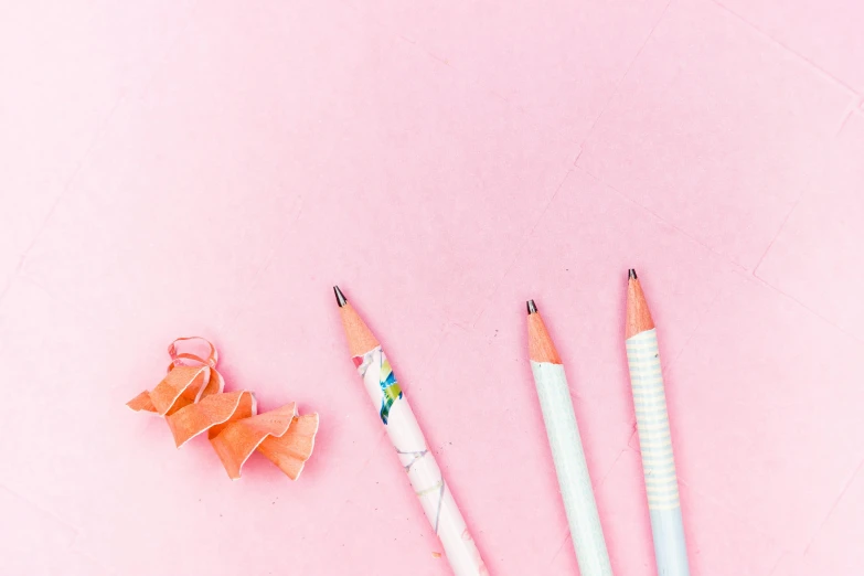 a couple of pencils sitting on top of a pink surface, trending on pexels, swirly tubes, background image, paper origami, bows