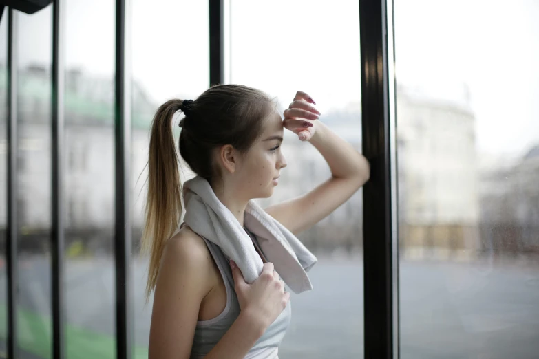 a woman standing in front of a window with a towel on her head, pexels contest winner, wearing a vest top, waist reaching ponytail, wearing a tracksuit, profile image