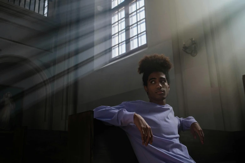 a man sitting on a bench in front of a window, pexels contest winner, mannerism, lilac sunrays, with afro, standing in a church, serious lighting
