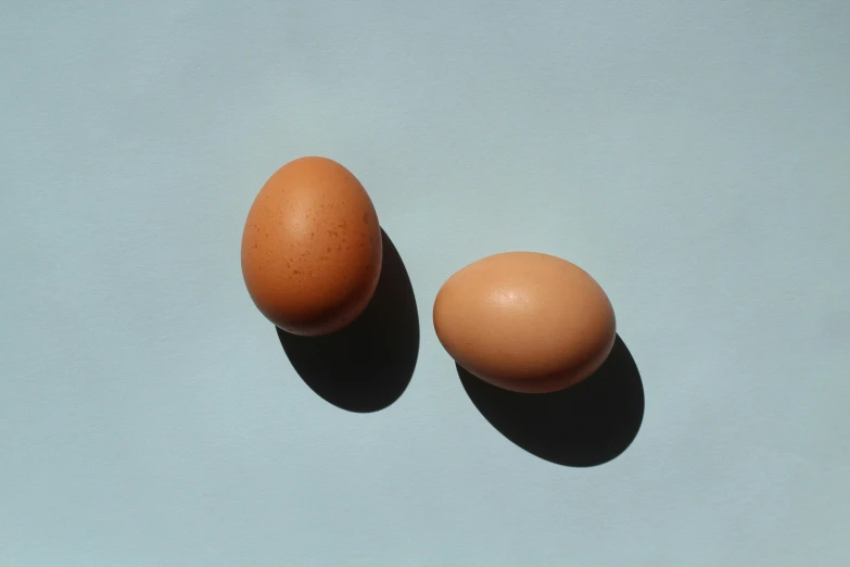 two eggs sitting next to each other on a blue surface, trending on pexels, 🦩🪐🐞👩🏻🦳, light tan, profile pic, background image