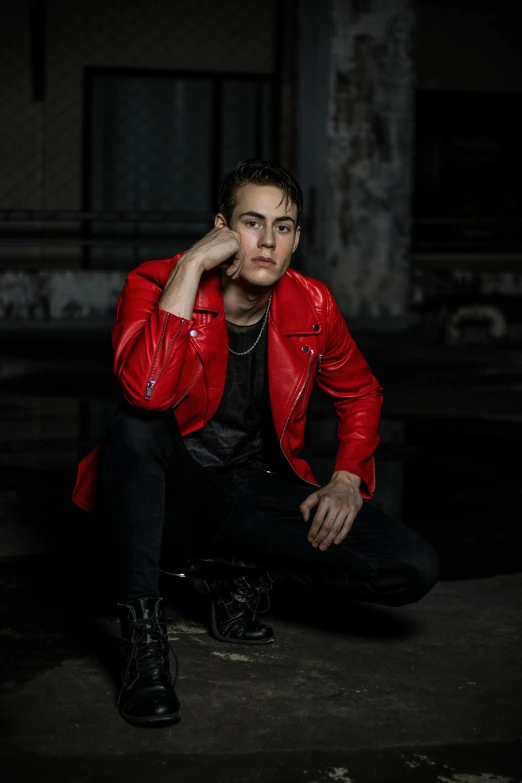 a man in a red jacket sitting on the ground, an album cover, by Cosmo Alexander, pexels contest winner, bauhaus, wearing leather jacket, profile image, ryan dyar, an epic non - binary model