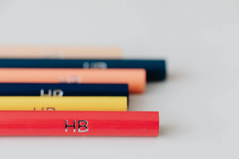 a row of colored pencils with the word hb on them, by Hermione Hammond, unsplash, hyperrealism, coloured in blueberra and orange, product design shot, on grey background, holly bruce