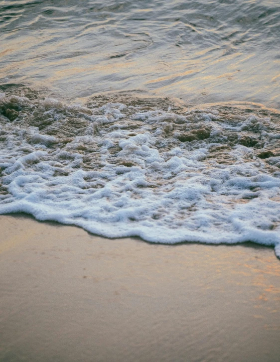a person riding a surfboard on top of a sandy beach, upclose, in water, in the evening, water flowing