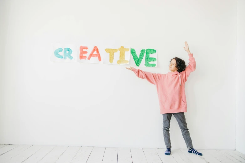 a little girl holding up a sign that says creative, pexels, interactive art, background image, wall painting, creative fashion, thumbnail