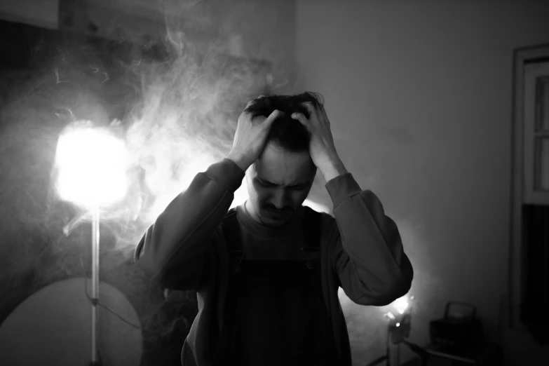 a black and white photo of a man holding his hair, a black and white photo, by Adam Marczyński, pexels, renaissance, smoke filled room, depressed, set photograph, poorly lit