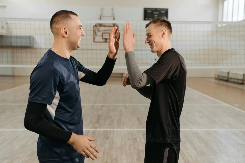a couple of men standing on top of a wooden floor, volleyball net, vitaly bulgarov and mike nash, hands in air, background image
