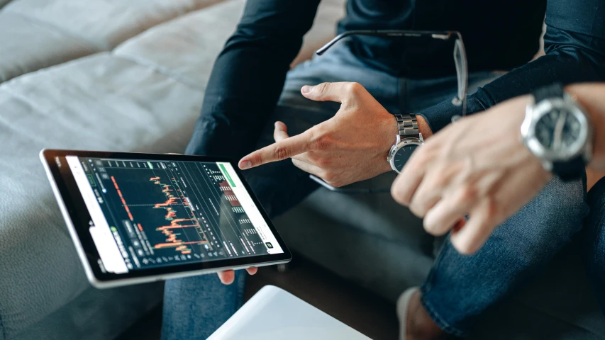 two people sitting on a couch looking at a tablet, trending on pexels, analytical art, displaying stock charts, hand on table, liam brazier, pointing