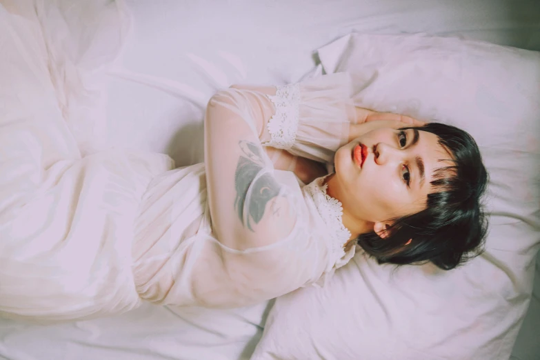 a woman in a white dress laying on a bed, inspired by Elsa Bleda, trending on pexels, visual art, melanie martinez, of taiwanese girl with tattoos, translucent white skin, white sleeves