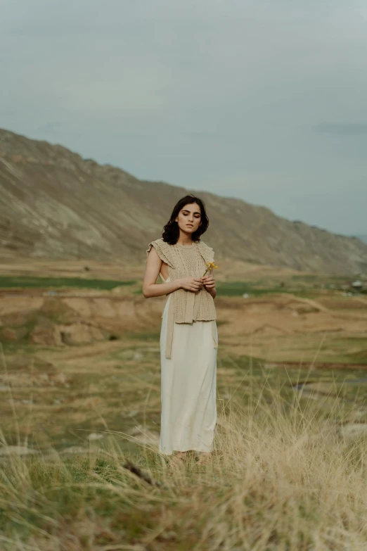 a woman standing on top of a grass covered field, by irakli nadar, holding a bottle of arak, simple cream dress, ash thorp khyzyl saleem, portrait image