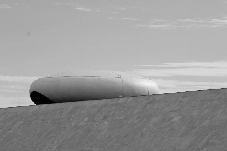 a man riding a skateboard up the side of a ramp, a black and white photo, inspired by René Burri, unsplash contest winner, minimalism, futuristic dome, rounded roof, lone industrial!!! spaceship!!, nazare (portugal)