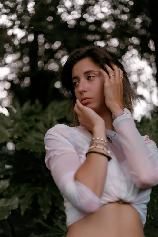 a woman in a white shirt talking on a cell phone, a colorized photo, inspired by Elsa Bleda, trending on pexels, renaissance, wearing two silver bracelets, looking majestic in forest, thoughtful pose, androgynous person