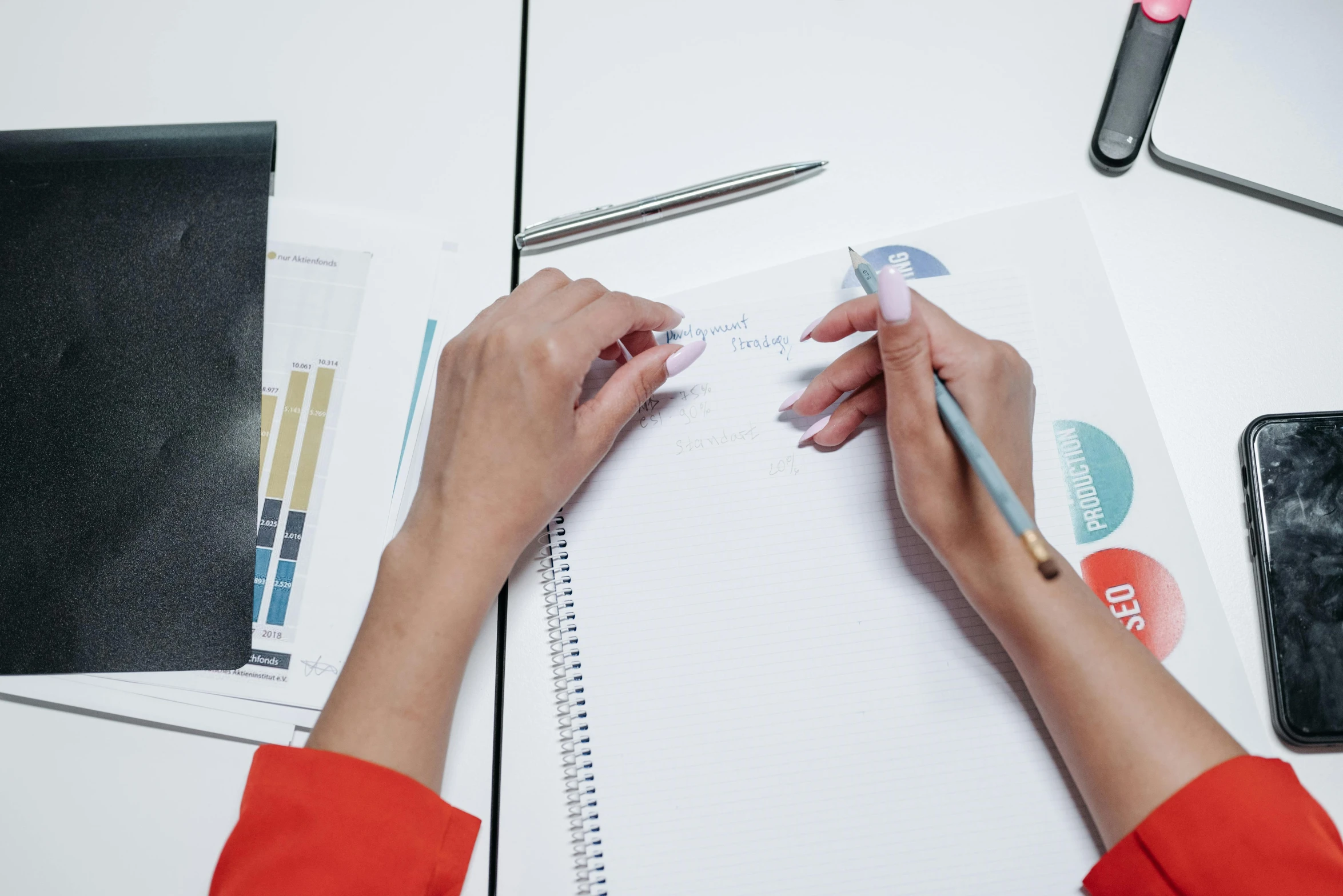 a woman sitting at a desk writing on a piece of paper, by Nicolette Macnamara, pexels contest winner, analytical art, 9 9 designs, red writing, charts, holding notebook