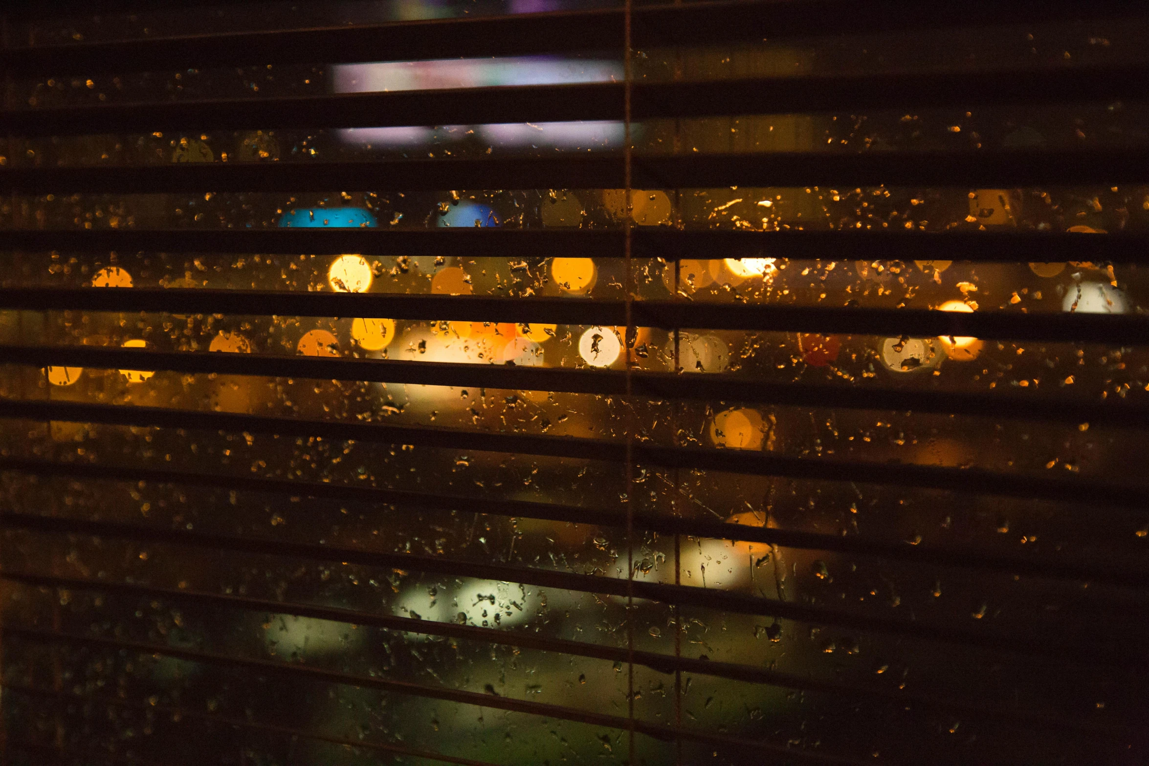 a close up of a window with rain on it, inspired by Elsa Bleda, warm yellow lights, soft light through blinds, golden orbs and fireflies, dark and moody