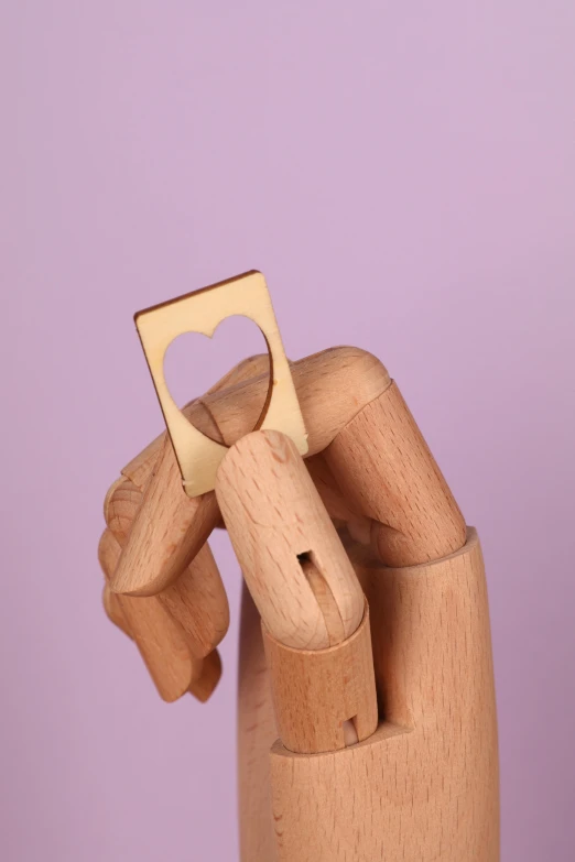 a wooden hand holding a bottle opener with a heart on it, gold plated, detail shot, geometric, rectangle