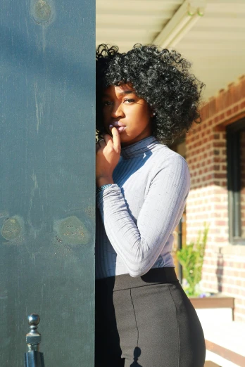a woman standing in front of a door talking on a cell phone, an album cover, by Lily Delissa Joseph, unsplash, black turtleneck, with curly black and silver hair, hiding behind a brick wall, black teenage girl