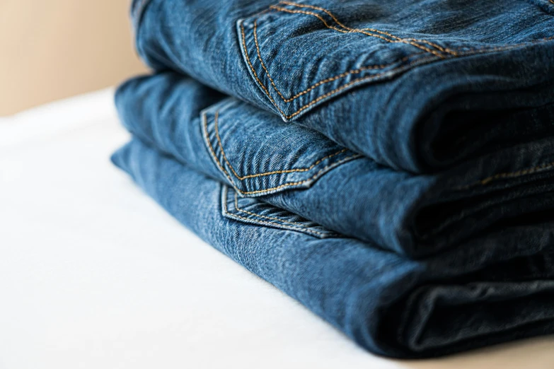 a stack of blue jeans sitting on top of a white table, by Nina Hamnett, trending on unsplash, detail shot, award - winning crisp details, patterned, three views