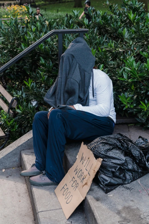 a person that is sitting on some steps, hood covers his eyes, belongings strewn about, a friend in need, uncropped