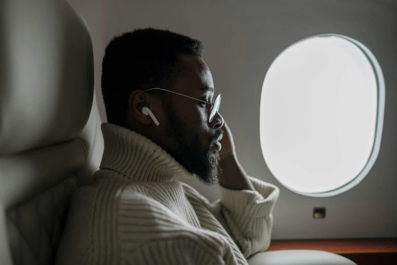 a man sitting in an airplane talking on a cell phone, by Jessie Algie, pexels contest winner, afrofuturism, earbuds jewelry, donald glover, slightly minimal, view from the side”