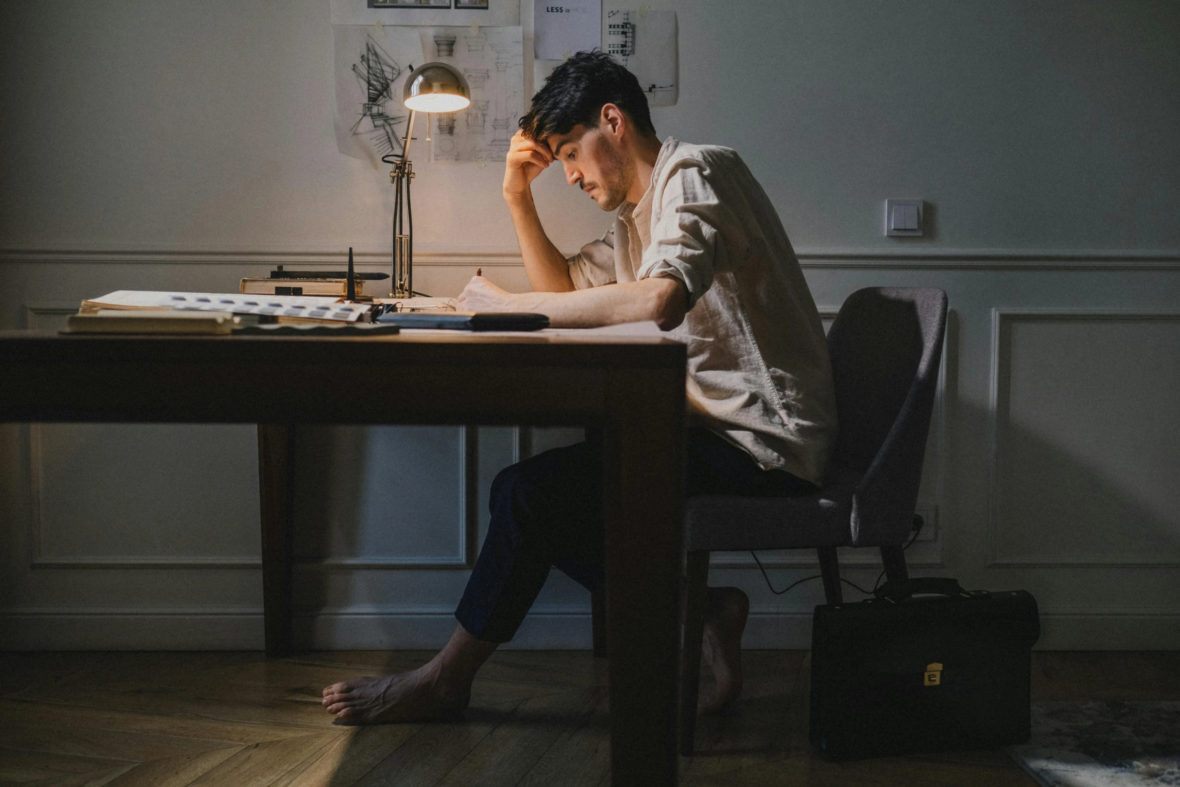 a man sitting at a desk in front of a lamp, a drawing, by Alexander Runciman, pexels contest winner, looking exhausted, asian male, sitting on bent knees, drawing pictures on a notebook