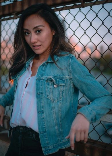 a beautiful young woman leaning against a fence, by Robbie Trevino, wearing a jeans jackets, mai anh tran, front lit, promo image