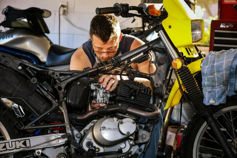 a man working on a motorcycle in a garage, lachlan bailey, yellow, profile image, repairing the other one