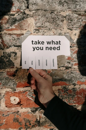 a person holding a sign that says take what you need, unsplash, concrete poetry, instagram post, labels, painted on a brick wall