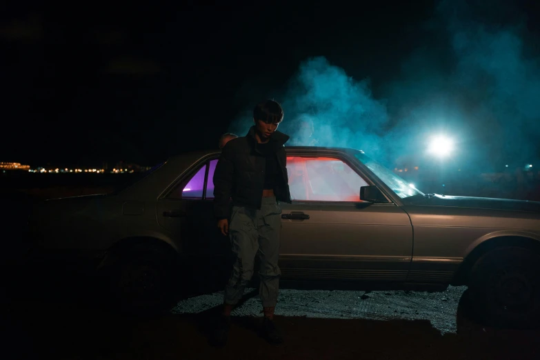 a man standing next to a car with smoke coming out of it, an album cover, by Elsa Bleda, pexels contest winner, realism, bisexual lighting, burning wrecked mercedes 1 2 4, yung lean, 80s outrun