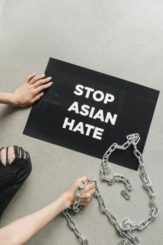 a woman is chained to a sign that says stop asian hate, a poster, trending on unsplash, flatlay, no cropping, gay rights, hindu