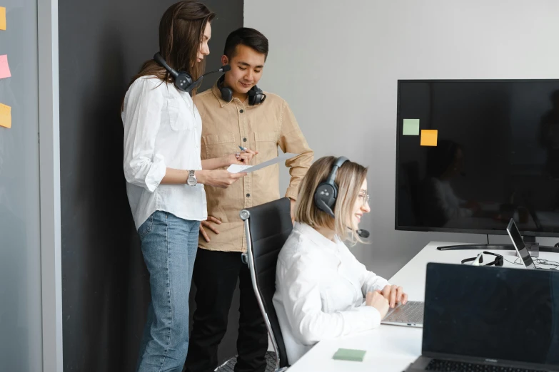 a group of people standing in front of a computer, with head phones, on a gray background, sat at a desk, 🦑 design