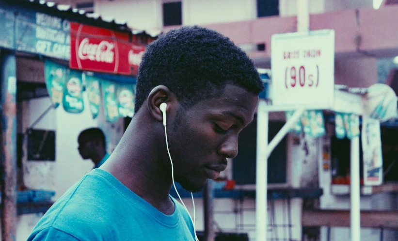 a man in a blue shirt is looking at his cell phone, an album cover, by Chinwe Chukwuogo-Roy, pexels contest winner, earbuds, faded color, cinematic. ”, baleful young