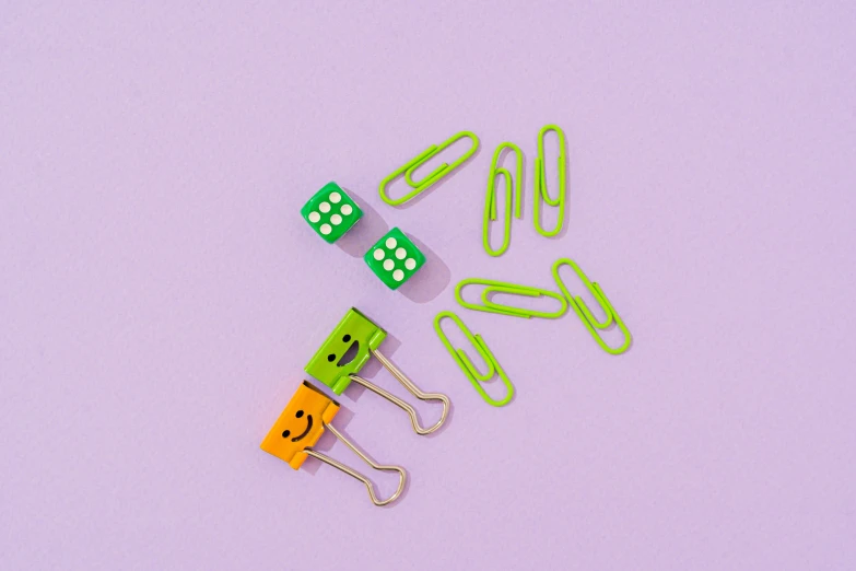 a couple of paper clips sitting next to each other, trending on pexels, lots of dices everywere, purple green color scheme, subject is smiling, various items