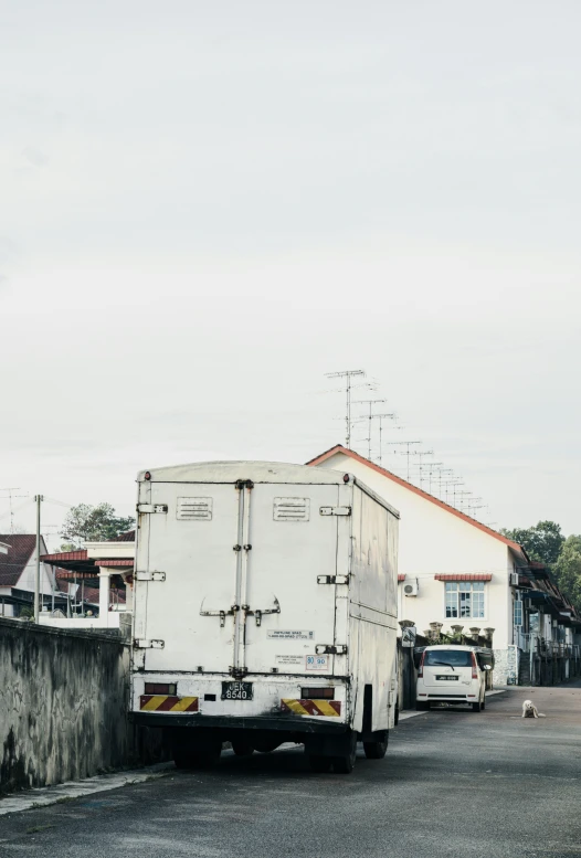 a white truck driving down a street next to a wall, unsplash, malaysian, low quality photo, back turned, caravan