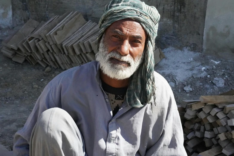 a man sitting in front of a pile of wood, a portrait, pexels contest winner, les nabis, made of cement, an afghan male type, grey mustache, unedited