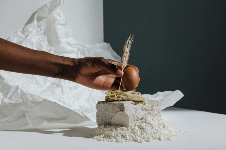 a person holding an egg on top of a pile of flour, a marble sculpture, inspired by Richmond Barthé, natural materials, plating, product introduction photo