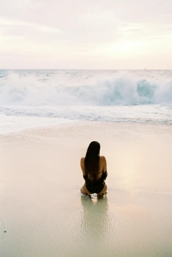 a woman sitting on top of a beach next to the ocean, unsplash, minimalism, tall backlit waves, back turned, waikiki beach, battered