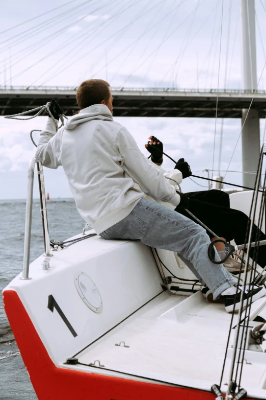 a man sitting on the bow of a sailboat, happening, on a bridge, ready to strike, grey, wearing a fancy jacket