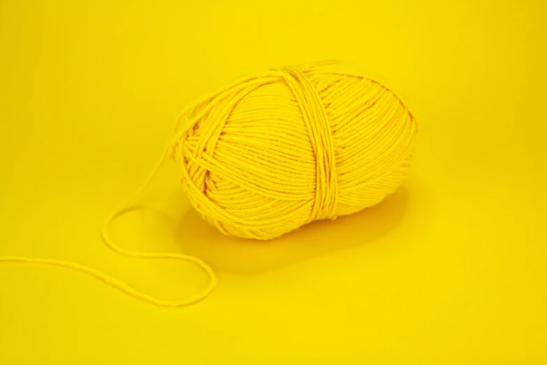 a ball of yarn on a yellow background, by Toss Woollaston, pexels contest winner, yellow artificial lighting, banana color, set against a white background, crafting