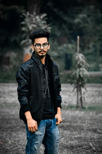 a man standing in a field with a skateboard, inspired by Saurabh Jethani, pexels contest winner, wearing black frame glasses, wearing a black jacket, harsh good looking face, wearing jeans and a black hoodie