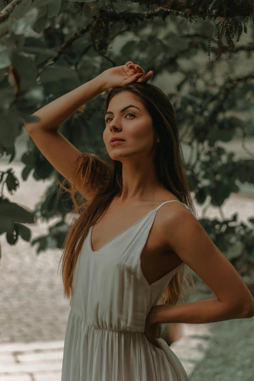 a woman in a white dress standing under a tree, inspired by Elsa Bleda, pexels contest winner, renaissance, wearing tank top, attractive brown hair woman, confident relaxed pose, her hair is tied above her head