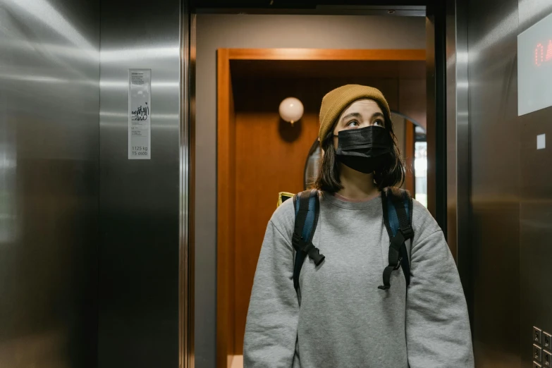 a woman wearing a face mask standing in an elevator, pexels contest winner, with black beanie on head, pokimane, student, hotel room