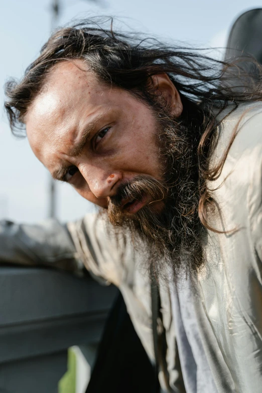 a man with long hair leaning on the back of a truck, bigger forehead, dirty beard, ( ( theatrical ) ), square