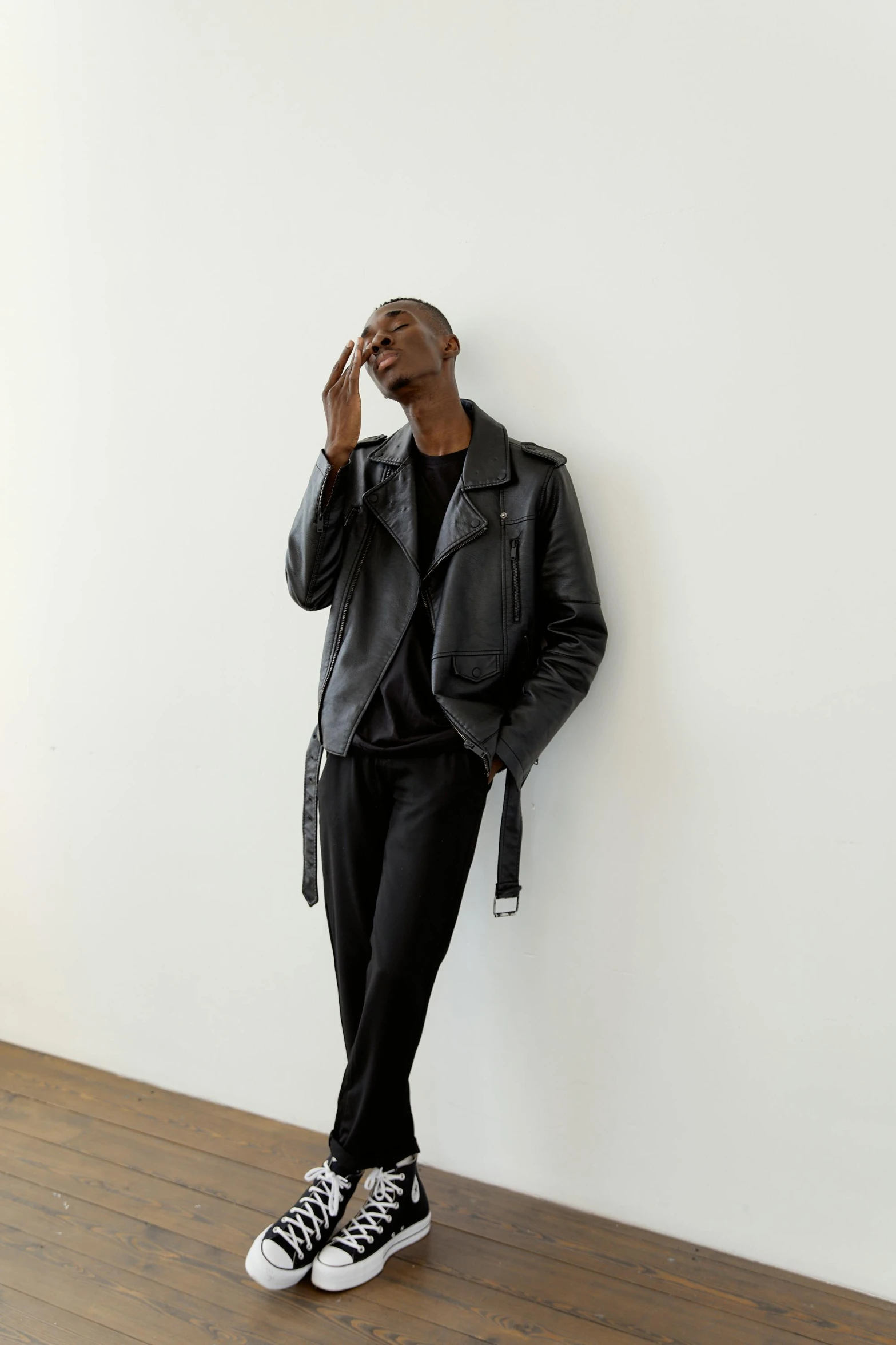 a man in a black jacket leaning against a wall, off - white collection, black jacket | shiny, dark skinned, f / 2 0