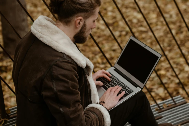 a man sitting on a bench using a laptop computer, trending on pexels, wearing a brown cape, scruffy man, autumn, student