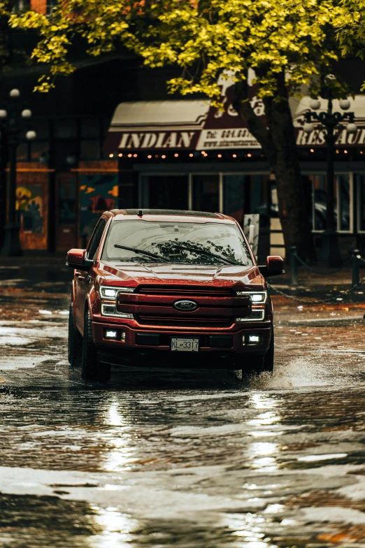 a red truck driving down a wet street, unsplash contest winner, photorealism, ford, reddish exterior lighting, square, indian