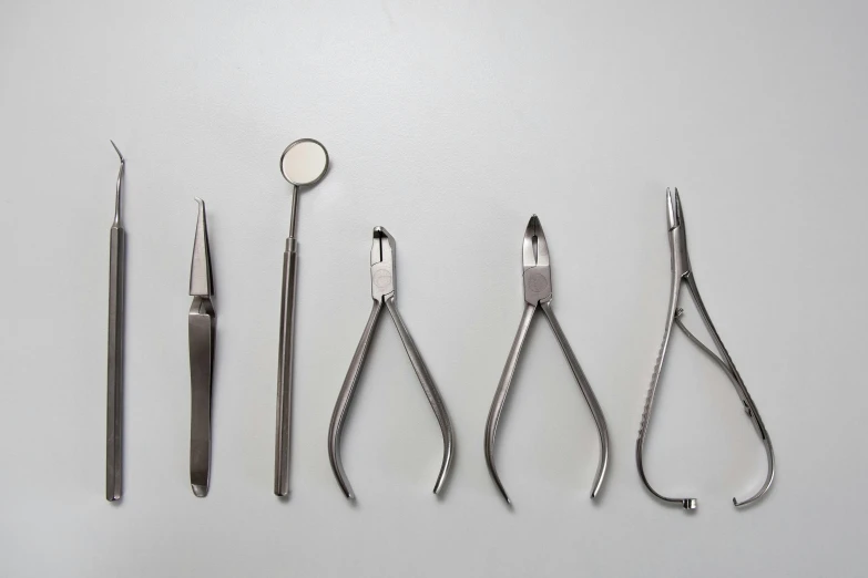 a group of tools sitting on top of a white surface, surgical impliments, only five fingers, stainless steal, dentils